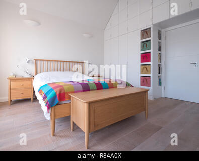 Style Scandi, minimaliste, dépouillé de l'intérieur chambre à coucher avec des meubles de chambre à coucher en bois, murs peints en blanc, des draps blancs, et des paniers de raphia coloré Banque D'Images