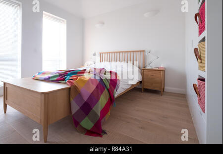 Style Scandi, minimaliste, dépouillé de l'intérieur chambre à coucher avec des meubles de chambre à coucher en bois, murs peints en blanc, des draps blancs, et des paniers de raphia coloré Banque D'Images