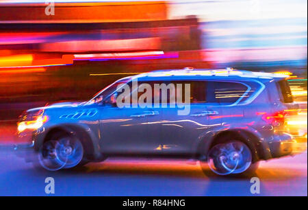 La longue exposition impressionniste shot d'une voiture pleine de jeunes gens sur la lumière d'une ville au crépuscule Banque D'Images