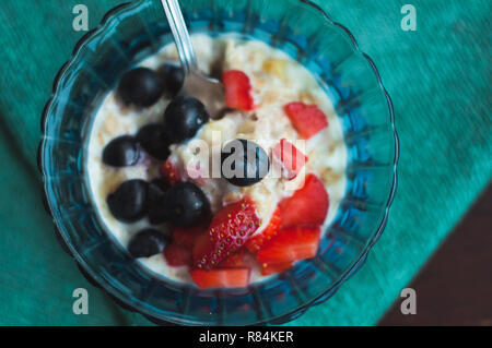 High angle view sur l'avoine cuits avec des fruits de la forêt. Les fraises et les bleuets dans un bol en verre bleu sur une serviette verte. Banque D'Images