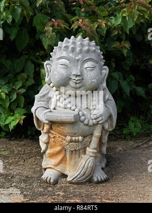 Sourire mignon Statue de Bouddha japonais avec grand cordon Collier et balai sur fond vert Feuilles Banque D'Images