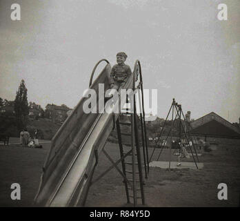 Années 1950, historique, un jeune garçon assis à l'extérieur sur le dessus d'un métal aire de glisse, en Angleterre. Banque D'Images