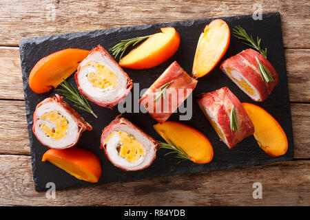 Belle alimentation : rouleau de porc cuit dans le prosciutto et fromage farci de kaki et gros plan sur la table. Haut horizontale Vue de dessus Banque D'Images