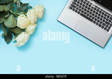 Bureau avec ordinateur portable et femme rose blanc bleu fleurs sur table. Vue de dessus la composition avec copie espace. Banque D'Images