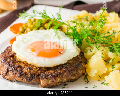 Émincé avec œuf frit et sa purée de pommes de terre sur la plaque blanche sur table en bois brun foncé dans le Banque D'Images