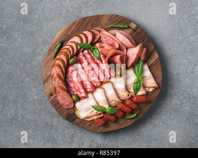 L'antipasto platter ensemble sur plaque de bois en pierre grise. Viande fumée froide plaque avec de la saucisse, des tranches de jambon,jambon,bacon, olives noires, basilic. Apéritif sur plateau en bois arbre scié l'imitation. Copier l'espace. Vue d'en haut Banque D'Images