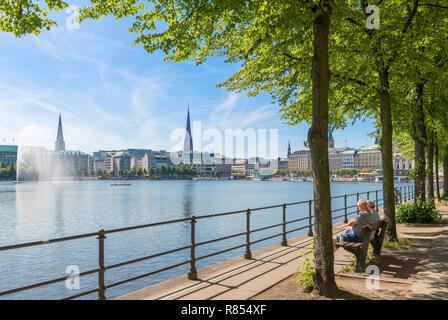 Couple assis sur un banc au bord de la lac Binnenalster avec l'horizon de la ville derrière, Hambourg, Allemagne Banque D'Images