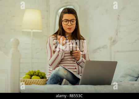 Attendez un bébé. La femme enceinte de manger le chocolat dessert et surfer sur l'internet Banque D'Images