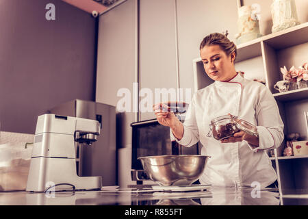 Chef pâtissier. Femme sérieuse Nice ajouter le cacao à la farine tout en se concentrant sur son travail Banque D'Images