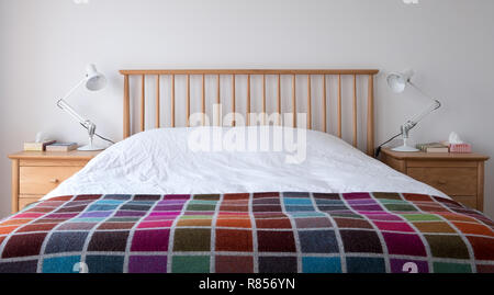 Style Scandi, minimaliste, dépouillé de l'intérieur chambre à coucher avec des meubles de chambre à coucher en bois, murs peints en blanc, des draps blancs et une couverture en couleur. Banque D'Images