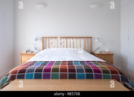 Style Scandi, minimaliste, dépouillé de l'intérieur chambre à coucher avec des meubles de chambre à coucher en bois, murs peints en blanc, des draps blancs et une couverture en couleur. Banque D'Images