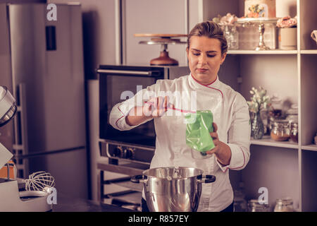 Meilleur Pâtissier. Belle femme qualifiée à l'aide d'une spatule professionnelle tout en mettant la crème dans la poche à pâtisserie Banque D'Images