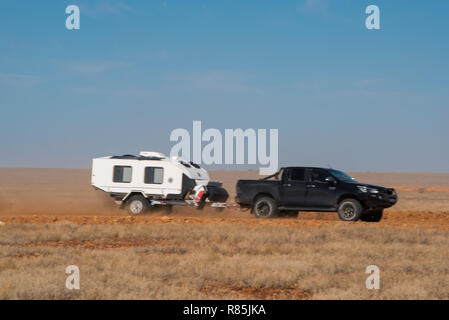 Noir, 4x4 Toyota Hilux hors route remorquage caravane sur l'arrière-pays australien-rouge route de terre avec ciel bleu et de la poussière. Banque D'Images