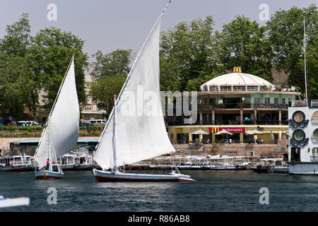 Felouques égyptiennes (bateaux) naviguer sur le Nil, passé l'American restaurant fast-food McDonald's, à Assouan, Egypte. Banque D'Images