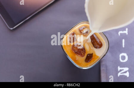 Verser le lait dans un verre de café glacé glaçons sur fond sombre. lettres numéro 1 et tablette Banque D'Images