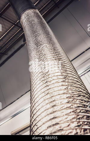 Air-conditionné métallique extensible tuyau de ventilation ou un tube de monter jusqu'au plafond à l'intérieur d'une unité de type industriel gris ou de l'usine Banque D'Images