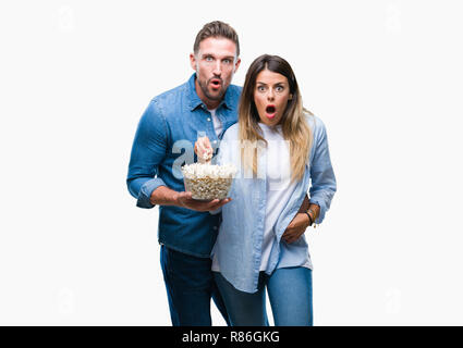 Jeune couple amoureux eating popcorn sur fond isolé en peur avec une surprise de Choc Visage, peur et excité par la peur d'expression Banque D'Images