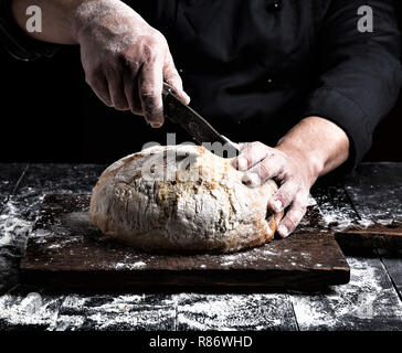 Coupe homme avec un couteau à pain de toute une partie de la farine de blé blanche sur une planche en bois brun Banque D'Images