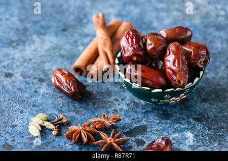 Dates et épices cardamome, l'anis étoile, bâtons de cannelle, girofle, sur un fond noir en bleu. Banque D'Images