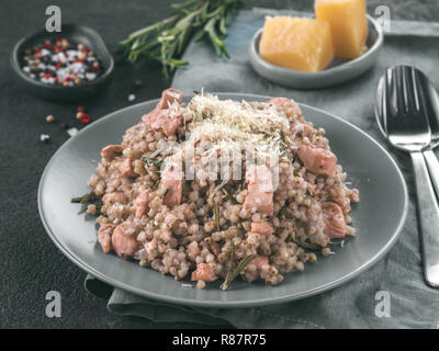 Le sarrasin cru risotto à la viande de poulet et fromage parmesan romarin servi en gris sur fond noir de la plaque de ciment. Sarrasin sans gluten et des idées recettes. Copier l'espace. La tonalité de l'image. Banque D'Images