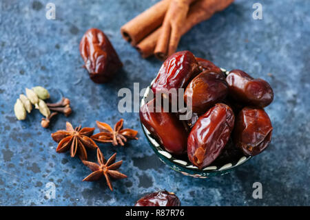 Dates et épices cardamome, l'anis étoile, bâtons de cannelle, girofle, sur un fond noir en bleu. Banque D'Images