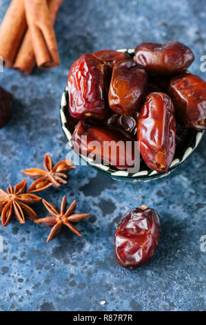Dates et épices cardamome, l'anis étoile, bâtons de cannelle, girofle, sur un fond noir en bleu. Banque D'Images