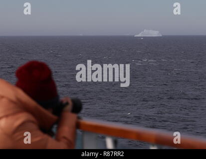 Grönland Disko Bucht: Keuzfahrtgast fotografiert einen Eisberg, er stützt sich auf der Reling ab, weil der Wind sehr stürmisch ist. Banque D'Images