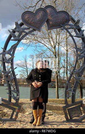 Couple aimant à valentines day dans un parc de la ville contre un lac sous un grand coeur forgé Banque D'Images