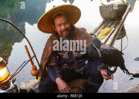 Cormorant fisherman holding chinois oiseau cormoran sur bras sur radeau dans le lac de Guilin, Chine. Fisherman in et le cap, a lanterne sur le radeau. Banque D'Images