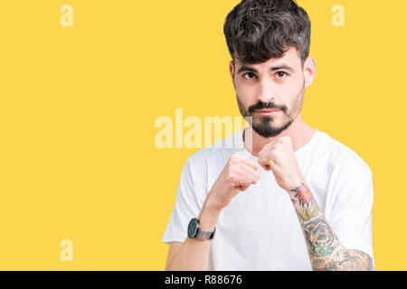 Beau jeune homme portant un t-shirt blanc sur fond isolé prêt à combattre avec fist, geste de défense en colère et contrarié face, peur de problème Banque D'Images