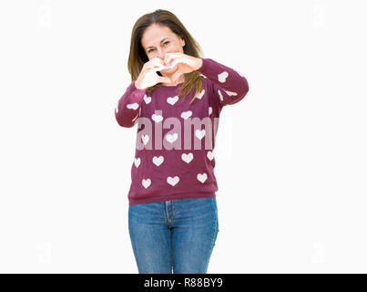 Belle femme d'âge moyen portant des cœurs isolés plus de pull en souriant en arrière-plan montrant l'amour du symbole du cœur et la forme des mains. Concept romantique Banque D'Images
