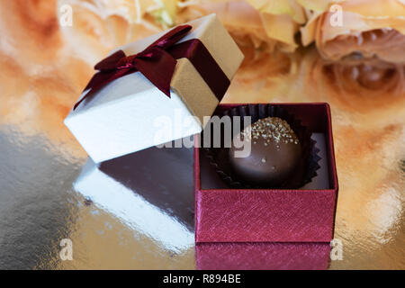 Bonbons au chocolat dans une boîte-cadeau. La boîte est sur une surface en argent sur l'arrière-plan de roses jaunes. Banque D'Images