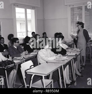 Années 1960, forieign étudiants assis à un bureau dans une salle de cours enseignés en anglais par une femme langues enseignant. Banque D'Images