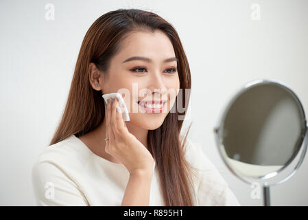 La prise de ses make-up. Belle jeune femme gaie avec disque pour coton et à son reflet dans le miroir avec sourire en coin à la robe Banque D'Images