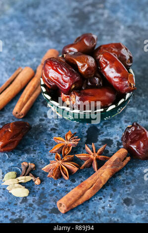 Dates et épices cardamome, l'anis étoile, bâtons de cannelle, girofle, sur un fond noir en bleu. Banque D'Images
