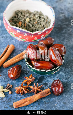 Dates, thé vert et épices cardamome, l'anis étoile, bâtons de cannelle, girofle, sur un fond noir en bleu. Banque D'Images
