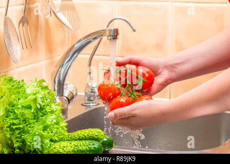Dans la cuisine, sous l'eau de lavage des mains de femmes de tomates mûres Banque D'Images