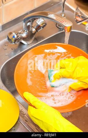 Laver la plaque orange avec une éponge en mousse avec des gants jaune sur la cuisine Vue de dessus Banque D'Images