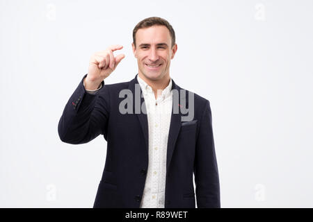 Un beau jeune homme avec une coiffure élégante montre une toute petite chose. Banque D'Images