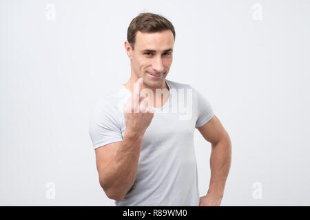 Beau jeune homme montrant viennent ici geste avec l'index et souriant sur fond gris. Banque D'Images
