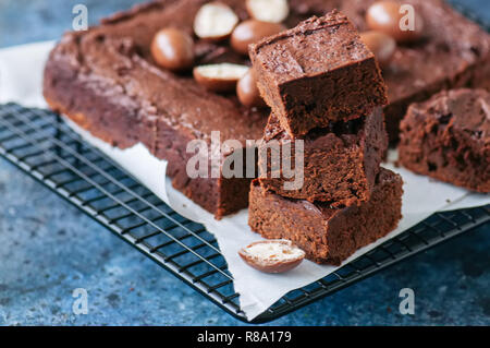 Brownie au chocolat noir sur une grille carrée décorée avec des oeufs en chocolat crémeux. Arrière-plan de pierre bleue. Banque D'Images