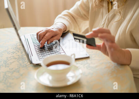 Focus sélectif d'un élégant ordinateur portable sur lequel un n'Achats en ligne. Tasse de thé trouble et une carte de crédit en main de femme sur l'avant-plan Banque D'Images