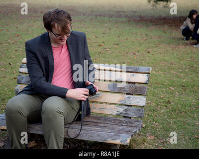 Un homme assis sur un banc de parc pour prendre des photos avec son appareil photo numérique Banque D'Images