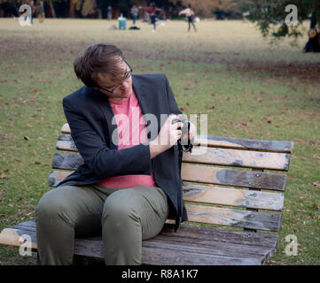 Un homme assis sur un banc de parc pour prendre des photos avec son appareil photo numérique Banque D'Images