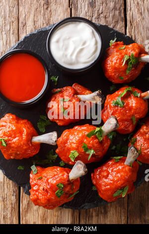 Sex apéritif Sucettes fried chicken wings rouge servi avec des sauces close-up sur une liste de sélection sur une table en bois. Haut Vertical Vue de dessus Banque D'Images