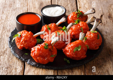 Alimentation populaire Lollipops rouge poêlé servi avec des sauces, les ailes de poulet sur une liste de sélection sur une table de bois horizontal. Banque D'Images