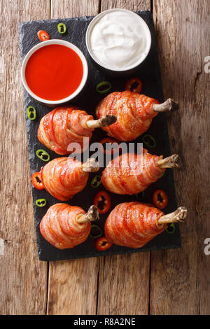 Sucettes délicieuses cuisses de poulet enrobé de bacon avec des sauces close-up sur une liste de sélection sur la table. Haut Vertical Vue de dessus Banque D'Images