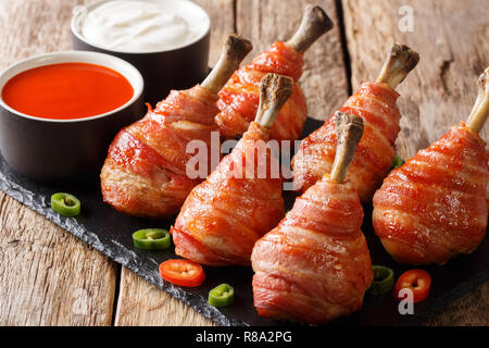Sucettes traditionnelles cuisses de poulet enrobé de bacon servi avec des sauces close-up sur une liste de sélection sur la table horizontale. Banque D'Images