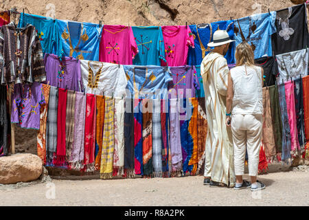 Une paire de touristes s'arrêter pour regarder les vêtements traditionnels colorés à vendre à Gorges de Todra, Tinghir, Maroc Banque D'Images