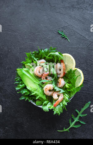 Salade de crevettes à l'avocat sur fond noir en noir, exemplaire de l'espace. Régime alimentaire sain salade verte aux crevettes (crevettes), d'avocat et de roquette. Banque D'Images